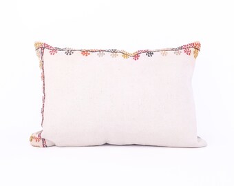 May include: A white pillow with a colorful embroidered border. The embroidery features a repeating pattern of small flowers in shades of red, orange, yellow, and green.