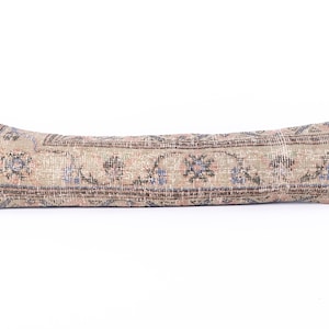 May include: A long, rectangular pillow with a floral pattern in shades of pink, blue, and green. The pillow is made from a woven fabric with a textured surface.