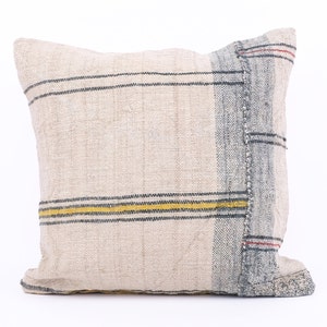 May include: A cream-colored throw pillow with a blue and yellow striped pattern. The pillow has a frayed edge and a textured fabric.