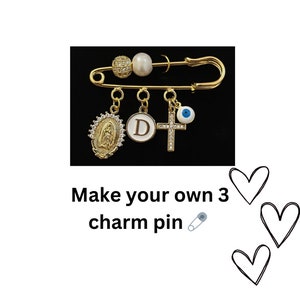 May include: Gold safety pin with three charms: a white pearl, a gold oval with a Virgin Mary image, a gold circle with the letter D, and a gold cross with a blue evil eye charm. Make your own 3 charm pin.