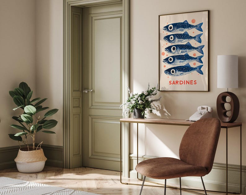 Może przedstawiać: Plakat w stylu vintage z białym tłem i czerwonymi k&oacute;łkami. Pięć niebieskich sardynek ułożonych pionowo, z napisem "SARDINES" nadrukowanym na czerwono poniżej. Plakat jest oprawiony i wisi na ścianie nad drewnianym stolikiem konsolowym.