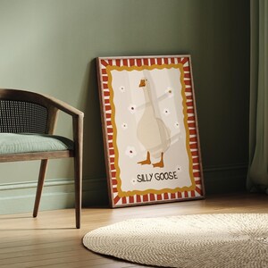 May include: A framed illustration of a white goose with red and yellow stripes around the border. The goose is standing with its wings outstretched and the text "Silly Goose" is printed below the goose.