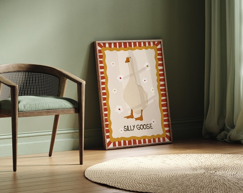 May include: A framed illustration of a white goose with red and yellow stripes around the border. The goose is standing with its wings outstretched and the text "Silly Goose" is printed below the goose.