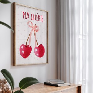 May include: A framed print with a pink background and white hearts. The print features two red cherries tied together with a pink ribbon. The text "MA CH&Eacute;RIE" is written in black at the top of the print.