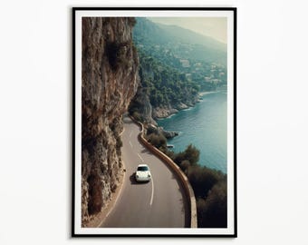 May include: Framed print of a white sports car on a coastal road. The road winds along a cliff face, offering views of the sea and a green hillside. The image has a vintage aesthetic, evoking travel and adventure.