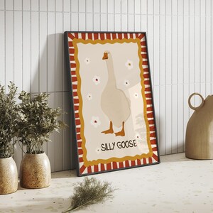 May include: A framed print with a white goose illustration on a cream background. The frame has a red and white striped border with a gold border. The text "Sally Goose" is printed in gold at the bottom of the print.