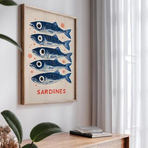 Może przedstawiać: Plakat w stylu vintage z niebiesko-białą ilustracją pięciu sardynek. Plakat ma jasną drewnianą ramę, a słowo "SARDYNKI" jest nadrukowane na dole na czerwono.