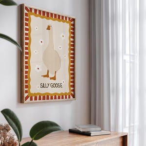 May include: A framed illustration of a white goose with red, yellow, and white stripes around the border. The text "Silly Goose" is printed in the center of the frame.