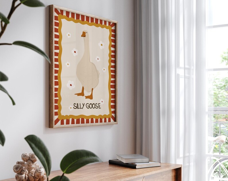May include: A framed illustration of a white goose with red, yellow, and white stripes around the border. The text "Silly Goose" is printed in the center of the frame.