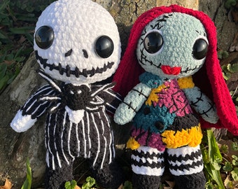 Könnte beinhalten: Zwei gehäkelte Plüschtiere, eines weiß mit schwarzen Streifen und einer schwarzen Schleife, das andere türkis mit roten Haaren und einem bunten Patchwork-Kleid, stehend vor einem Baumstamm.