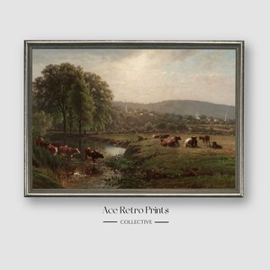 May include: A vintage painting depicting a pastoral scene with a stream running through a grassy field.  The painting features a group of brown and white cows grazing in the field.  The background shows a small village nestled in a valley.
