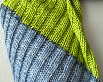 May include: A close-up of a hand-knitted scarf with a ribbed pattern. The scarf features sections of bright green, light blue, and a dark blue and purple section. The knitted texture is clearly visible.