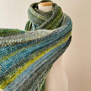 May include: A green, blue, and yellow striped knitted scarf with a subtle shimmer. The scarf is draped over a white mannequin.