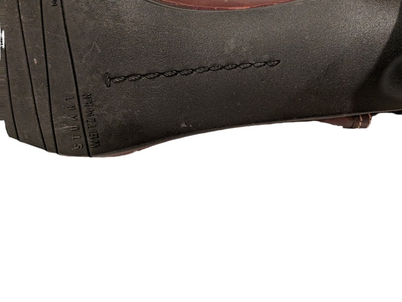 Pu&ograve; includere: Primo piano della suola di una scarpa in pelle marrone con il testo "STUART WEITZMAN" in rilievo.