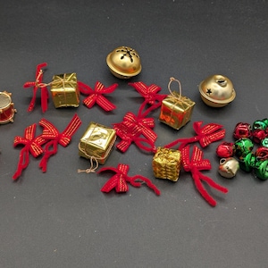 Puede incluir: Una colección de adornos navideños que incluye cajas de regalo doradas en miniatura, lazos de terciopelo rojo, campanas doradas y pequeñas campanas rojas y verdes. También hay dos tambores rojos en miniatura con detalles dorados.