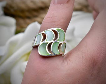 Puede incluir: Un anillo de plata con un patrón repetitivo de incrustaciones en forma de media luna de color verde pálido. La banda tiene un diseño ancho y calado con bordes de metal pulido que rodean cada segmento verde claro en una formación estructurada.