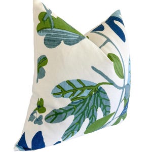 May include: A square cushion with a white base, adorned with a botanical design. The pattern showcases large leaves and stems in shades of blue and green. The cushion has a soft appearance, suitable for a living space.
