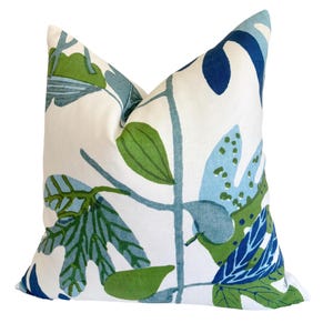 May include: Square cushion with a white backdrop and a botanical design of green, blue, and navy leaves and stems. The cushion has a soft, textured look and is likely made of fabric.