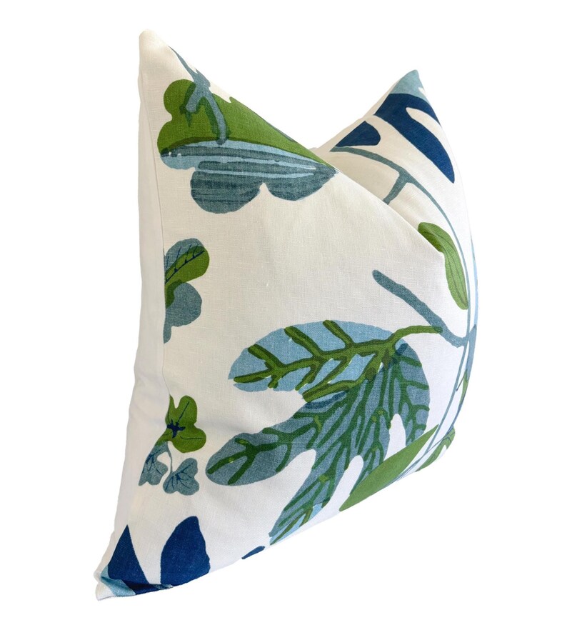 May include: A decorative cushion with a white backdrop and a botanical pattern in shades of blue and green. The cushion features large leaf and floral designs, adding a touch of nature-inspired decor to any living space. The cushion is a square shape.