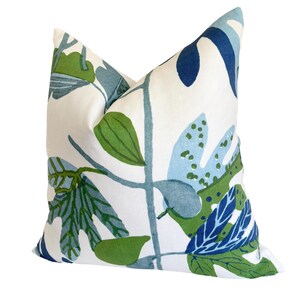 May include: A square cushion with a white backdrop and a botanical design. The pattern showcases green, blue, and navy leaves and stems. This cushion is a soft, comfortable accent piece for a sofa or bed.
