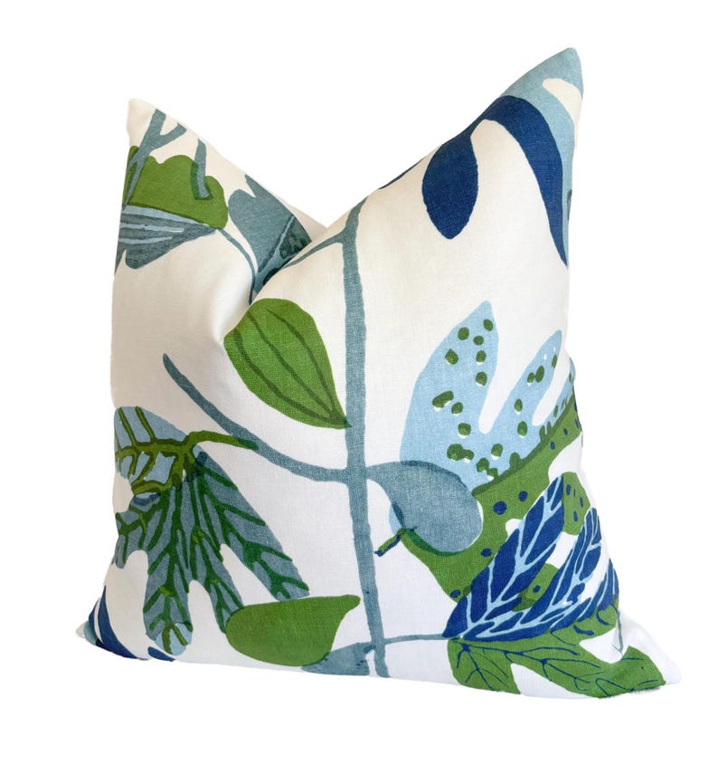May include: A square cushion with a white backdrop and a botanical design. The pattern showcases green, blue, and navy leaves and stems. This cushion is a soft, comfortable accent piece for a sofa or bed.