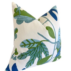 May include: A square cushion with a white base, adorned with a botanical design. The pattern showcases large leaves and stems in shades of blue and green. The cushion has a soft, inviting appearance, perfect for a sofa or bed.