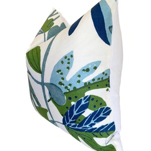 May include: A cushion with a white background and a botanical design. The pattern includes large leaves in shades of blue and green. The cushion has a plain white reverse.