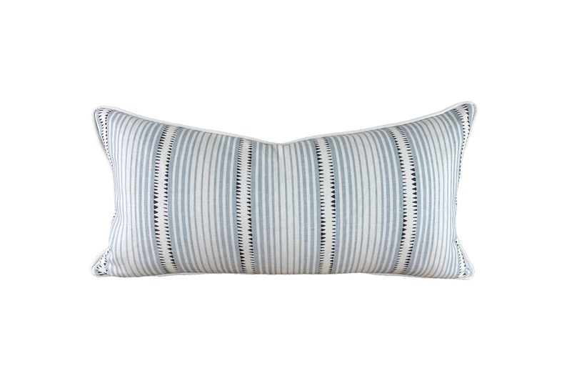 May include: A blue and white striped throw pillow with a white border. The pillow has a subtle pattern of small black triangles.