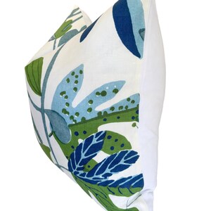 May include: A cushion with a white background and a botanical pattern in shades of blue and green. The cushion features large leaf designs and a plain white back.