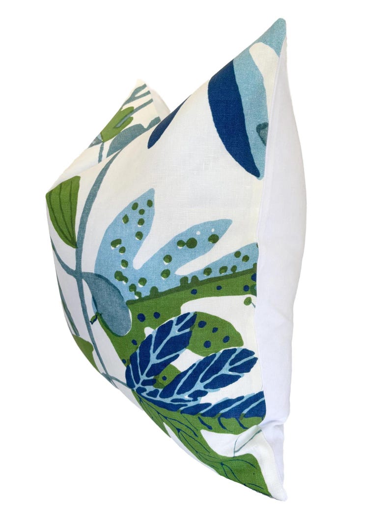 May include: A cushion with a white background and a botanical pattern in shades of blue and green. The cushion features large leaf designs and a plain white back.