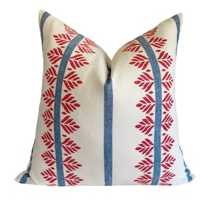 May include: A decorative throw pillow with a white background and a repeating pattern of red leaf-like shapes. The design is framed by two vertical blue stripes. The pillow is square and has a soft, inviting appearance.