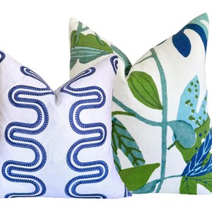May include: Two decorative cushions. One has a white background with a blue embroidered wavy pattern. The other has a white background with a green, blue, and teal botanical leaf design.