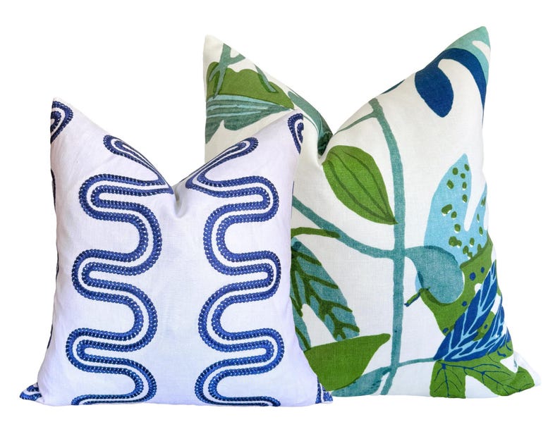 May include: Two decorative cushions. One has a white background with a blue embroidered wavy pattern. The other has a white background with a green, blue, and teal botanical leaf design.
