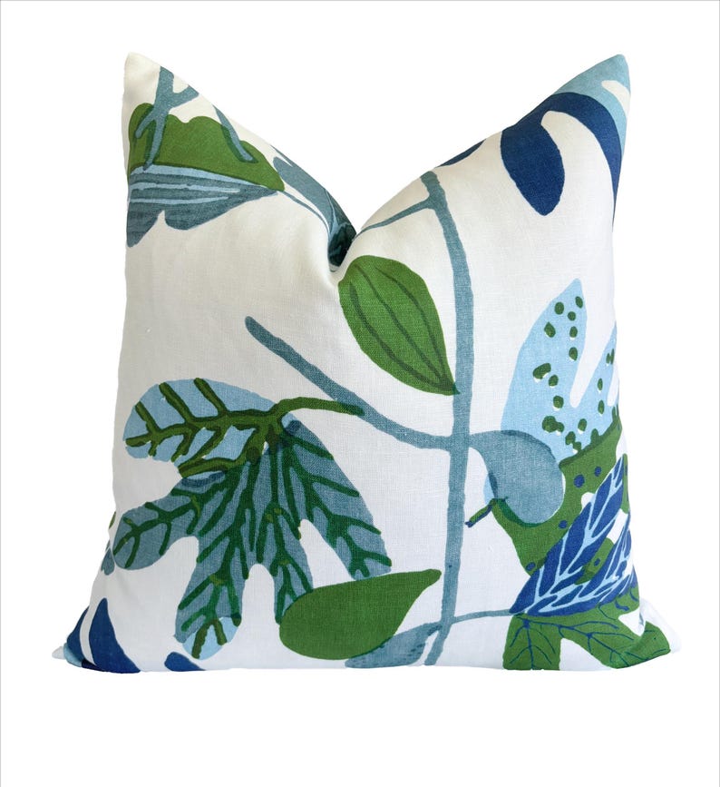 May include: A square cushion featuring a botanical leaf design in green and blue on a white background. The leaves are stylized and arranged in a repeating pattern. The cushion is a square shape, perfect for adding a touch of nature to any room.