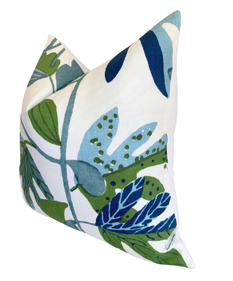 May include: A decorative cushion with a white backdrop and a botanical design. The pattern showcases large leaves in shades of green and blue. The cushion is square in shape.