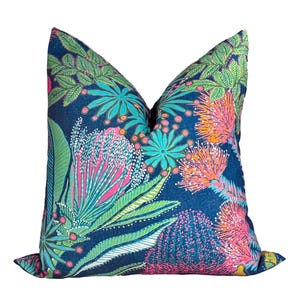 May include: A decorative throw pillow with a vibrant floral pattern. The pillow features a dark blue background with colorful botanical designs in shades of pink, green, orange, and teal. The pillow is a square shape.
