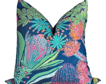May include: A decorative cushion with a striking floral design. The cushion has a dark blue backdrop, adorned with colourful botanical patterns in pink, green, orange, and teal. The cushion is square-shaped.