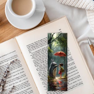 May include: A bookmark featuring a whimsical illustration of a furry, gray creature with large ears and a red umbrella. The creature is standing in a forest setting with green trees and a path. The illustration is painted in a realistic style with soft colors.