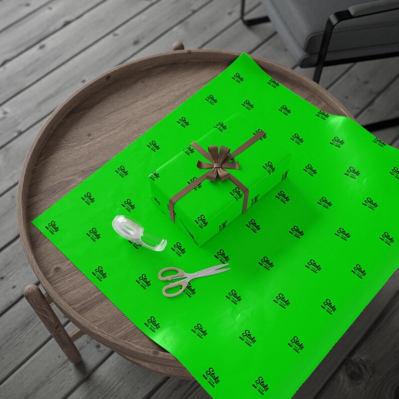 Pu&ograve; includere: Un regalo avvolto con un nastro marrone su carta da regalo verde brillante. La carta da regalo ha un motivo ripetuto di un logo nero. Un rotolo di nastro adesivo e forbici sono anche sulla carta da regalo.