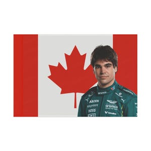 May include: A driver in a green racing suit with the Canadian flag in the background. The suit has the logos "Aramco", "Cognizant", "Boss", "Aramco Formula One Team", and "Valvoline" on it.
