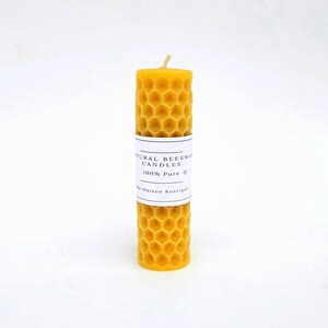 May include: A cylindrical, yellow beeswax candle with a honeycomb pattern. A white label wrapped around the candle reads "NATURAL BEESWAX CANDLES 100% Pure". The candle has a natural, rustic appearance and a wick at the top.