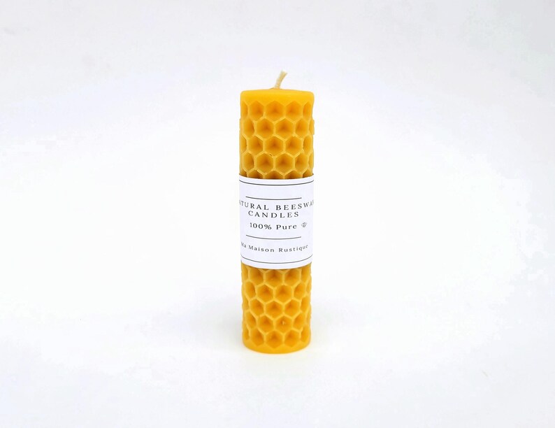 May include: A cylindrical, yellow beeswax candle with a honeycomb pattern. A white label wrapped around the candle reads "NATURAL BEESWAX CANDLES 100% Pure". The candle has a natural, rustic appearance and a wick at the top.