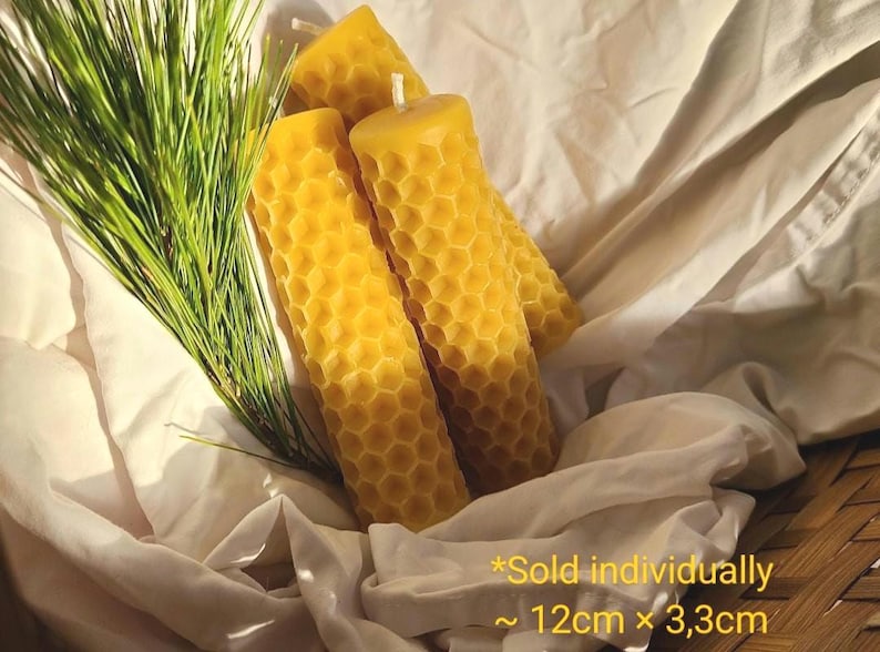 May include: Three yellow honeycomb-patterned candles with a white wick, resting on a white cloth. Green pine needles are to the left. The candles are approximately 4.7 inches tall and 1.3 inches wide.