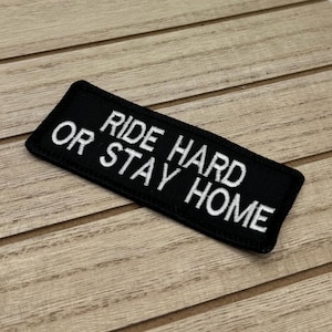 Op de afbeelding: Zwarte geborduurde patch met witte tekst die "Ride Hard Or Stay Home" luidt.
