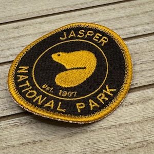 May include: A black and gold embroidered patch with the text "Jasper National Park Est. 1907" and a beaver silhouette.