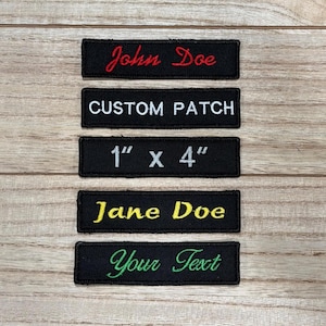 Può includere: Cinque toppe rettangolari nere ricamate con testo. La toppa superiore recita "John Doe" in corsivo rosso. La seconda toppa dice "CUSTOM PATCH" in maiuscolo bianco. La terza toppa dice "1" x 4"" in bianco. La quarta toppa dice "Jane Doe" in corsivo giallo. La toppa inferiore dice "Your Text" in corsivo verde.