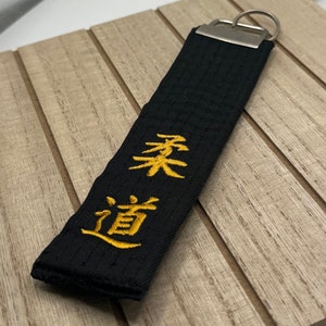 Può includere: Portachiavi nero con un designo ricamato in oro dei caratteri giapponesi "柔道" (Judo) e "柔" (Ju).