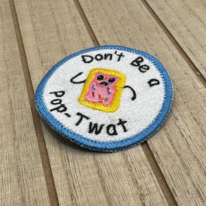 Può includere: Una toppa rotonda ricamata bianca con un bordo blu. La toppa presenta un Pop-Tart dei cartoni animati con una faccia e il testo "Don't Be A Pop-Tart".