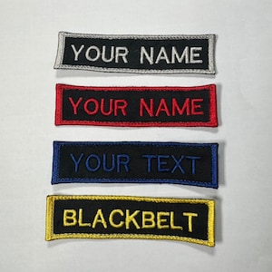 May include: Four embroidered patches with black fabric and different coloured borders. The patches read "YOUR NAME" in white, "YOUR NAME" in red, "YOUR TEXT" in blue, and "BLACKBELT" in yellow.
