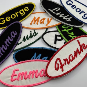 Peut inclure: Une collection d'étiquettes de nom ovales brodées de couleurs vives avec différents noms, dont George, Luis, May, Emma et Frank.